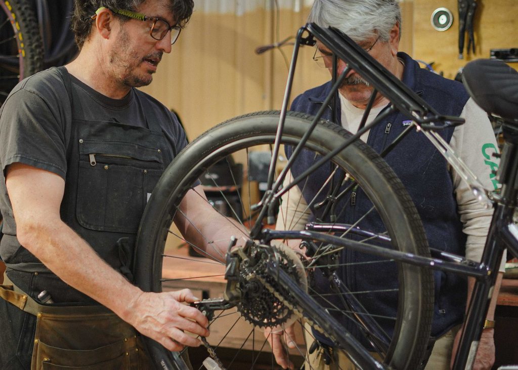 ryanandcustomer3 Ryan helps a customer reinstall the rear wheel and chain on a bike in the shop.