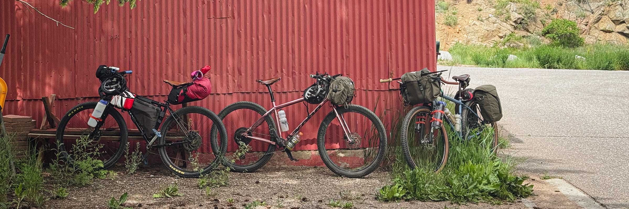 bikepacking_redbarn Three loaded bikepacking bikes leaning against a red corrugated wall.
